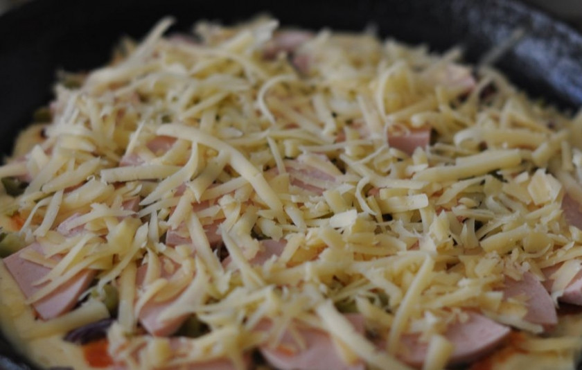 1. Этап. Пицца на сковороде с ветчиной: Ну а теперь начинка: сначала кладем нарезанный полукольцами лук, затем кружочки огурцов, наверх выкладываем ломтики ветчины. Посыпаем все тертым сыром.