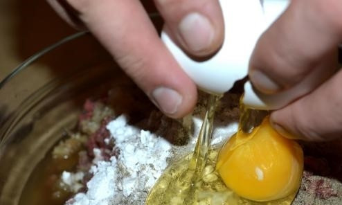 1. Этап. Колбаски из говядины: 4. Добавьте в фарш одно сырое яйцо. Влейте коньяк – 3 столовые ложки; или замените на водку (в том же количестве). Все тщательно перемешайте.