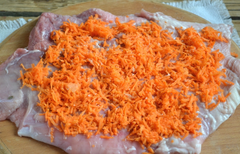 1. Этап. Новогодний рулет из свинины: На пласт мяса ровным слоем выложите натертую на мелкой терке сырую морковь, посолите. По желанию также можете использовать любимые специи. Главное — не переборщите с ними.
