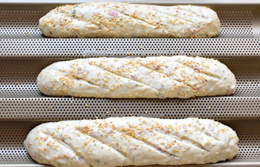 1. Этап. Французский хлеб с ветчиной: Сформуйте из каждой части пласт, который скрутите в плотный рулет, запечатывая каждый виток ладонью. Уложите сформованные багеты в форму или на лист. Смажьте багеты смесью яйца с молоком, сделайте несколько косых надрезов и по желанию посыпьте сверху кунжутом. Дайте расстояться минут 20.