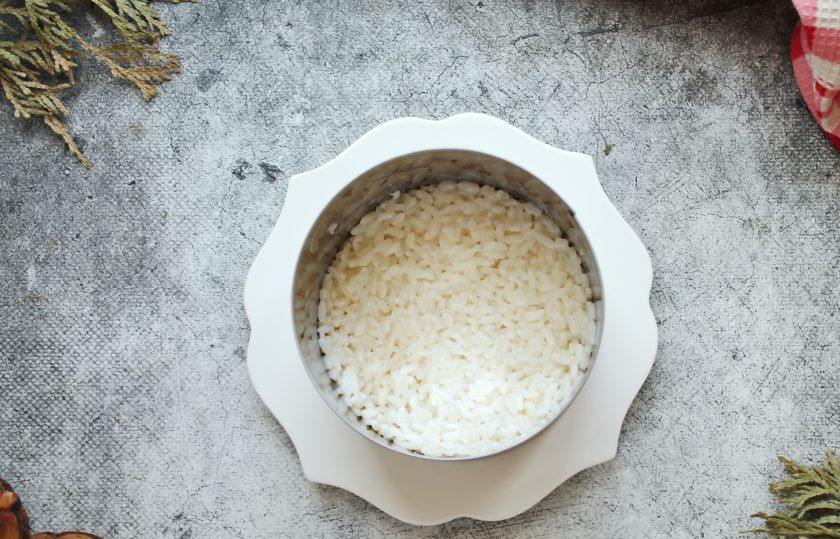 1. Этап. Салат Черное море: Смешайте отварной рис с частью майонеза и перемешайте. Кондитерское кольцо установите на сервировочное блюдо и выложите внутрь рис, утрамбуйте.