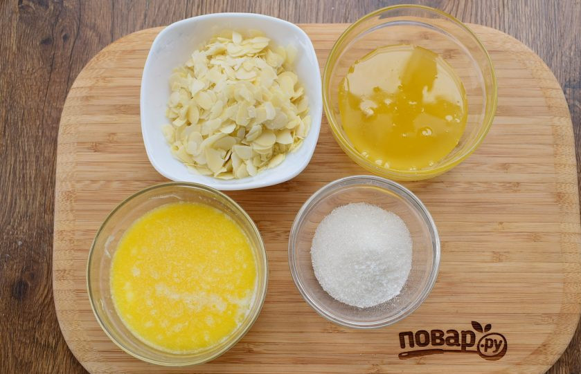 1. Этап. Медовый торт Пчелиный укус: Подготовьте необходимые продукты для медово-миндальной заливки. В кастрюльке с толстым дном или сотейнике соедините мед, сливочное масло, сахар и ванилин, доведите до кипения, варите на медленном огне в течение 1 минуты, добавьте миндальные хлопья (или рубленый миндаль) и перемешайте. Остудите до комнатной температуры.