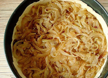 1. Этап. Луковый пирог из слоеного теста: Чуть больше половины теста раскатываем и укладываем в форму, смазанную маслом. Делаем небольшие бортики. Укладываем начинку на слой теста.