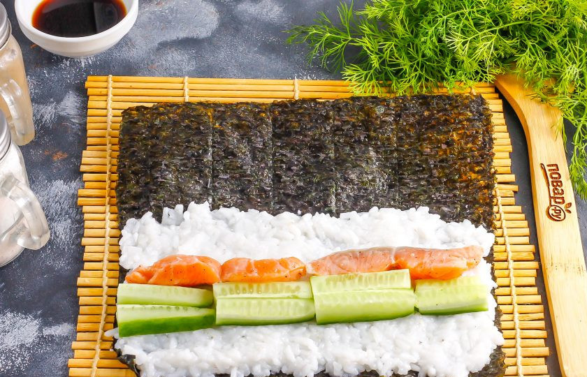 1. Этап. Спайси роллы: Выложите сливочный сыр, а на него — ломтики слабосоленой рыбы. Промойте огурец и срежьте хвостики, нарежьте длинными брусочками. Выложите на рыбу.