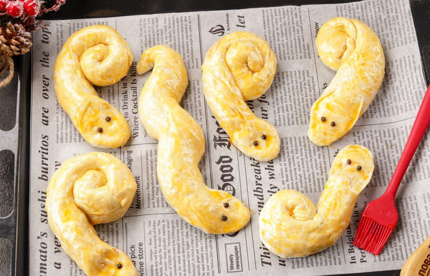 1. Этап. Новогодние пирожки Змейки: Придайте заготовкам форму змеек и выложите на противень, застеленный пергаментом. Я сделала змеек, свёрнутых калачиком, выкладывая тесто по спирали, переднюю часть оставила свободной и руками придала головам нужную форму. Вы можете придать любую другую форму вашим змейкам. Смажьте тесто желтком, а затем при помощи горошин чёрного перца или разрезанных изюминок сделайте глазки. Выпекайте в духовке при температуре 190 градусов до румяного цвета.