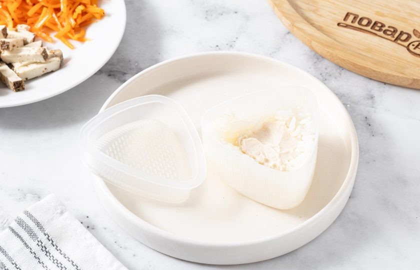 1. Этап. Онигири с корейской морковью: Смочите руки и формочку для онигири водой. Заполните форму наполовину, сделав углубление для начинки. В центр выложите немного сливочного сыра.