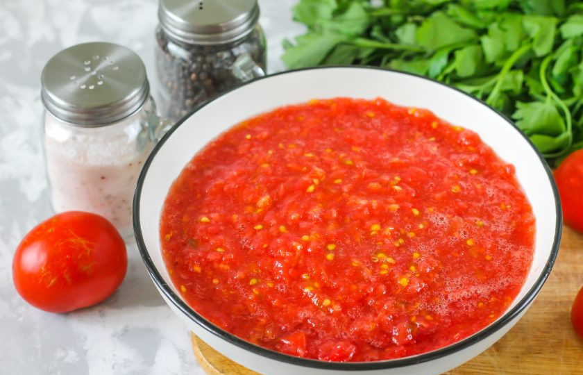 1. Этап. Заправка с перцем на зиму: Помидоры промойте в воде, разрежьте пополам и вырежьте зеленые черенки. Протрите половинки томатов через терку с мелкими ячейками в глубокую емкость.