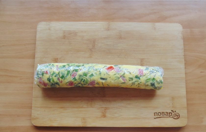 1. Этап. Рулет из омлета с овощами: Омлет немного охладите и достаньте из формы. Аккуратно сверните его рулетом и заверните в пищевую пленку. Дайте хорошо остыть.