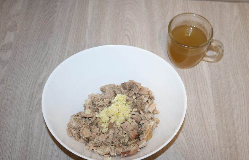 1. Этап. Домашний зельц из свиной рульки: К мясу добавьте чеснок, пропущенный через пресс, и влейте бульон с желатином. Хорошо всё перемешайте. По вкусу посыпьте прованскими травами.