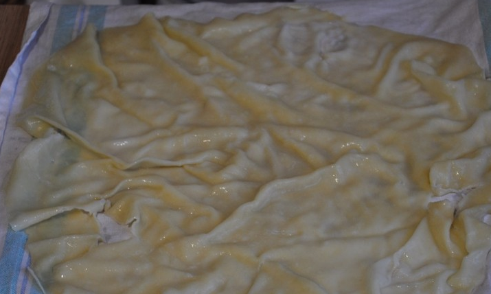 1. Этап. Ачма по-аджарски: Каждый отваренный кусок теста сразу же опускаем в кастрюлю с холодной водой. Затем раскладываем тесто на полотенце, чтобы стекла лишняя вода. Нижний слой теста выкладываем в форму для запекания (края теста должны свисать) и смазываем растопленным маслом. Таким же образом выкладываем еще два слоя теста. Сверху размещаем тертый сыр, затем — вновь несколько слоев теста с маслом и так далее.