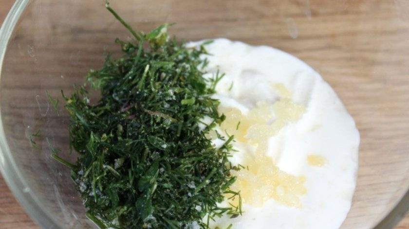 1. Этап. Слоеный салат с солеными огурцами: Вначале сделайте соус. Сметану смешайте с измельчённым укропом и чесноком, а также солью. Перемешайте.