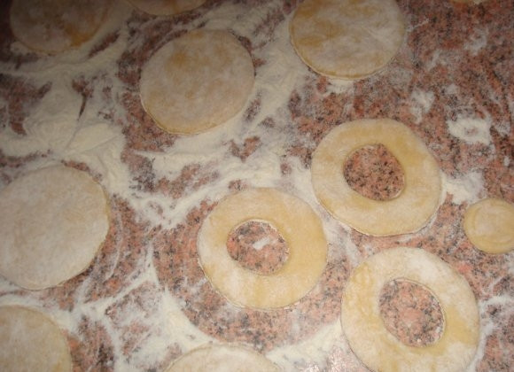 1. Этап. Московские пончики: Тесто скатайте в толстую колбаску и нарежьте её на кружочки толщиной около двух сантиметров. Рабочую поверхность присыпьте мукой и выложите кружочки, слека их приплюснув. Затем при помощи пробки от пластиковой бутылки вырежьте кругляши в тесте.