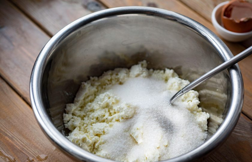 1. Этап. Вареники на кефире и дрожжах: Приготовьте начинку. Для этого поместите творог в отдельную миску, добавьте к нему 40 граммов сахара и все перемешайте ложкой.