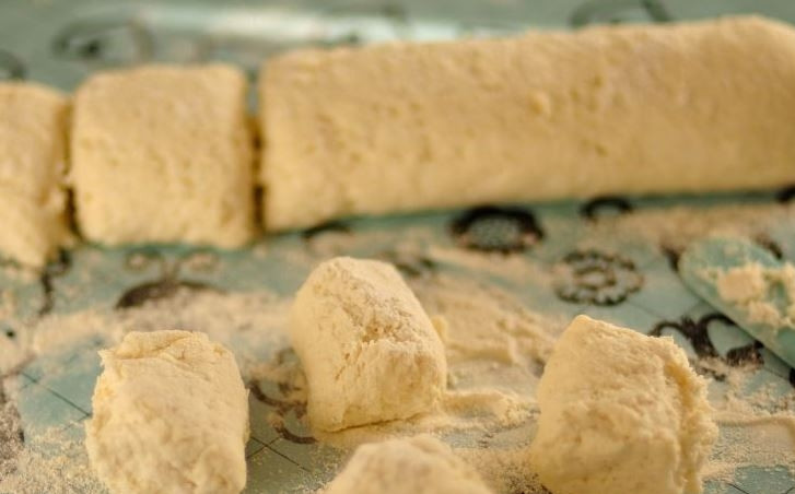 1. Этап. Сырники без жарки: Получившееся тесто выложите на рабочую поверхность и присыпьте его мукой. Скатайте из теста колбаску и разделите ее на шестнадцать небольших частей равного размера.