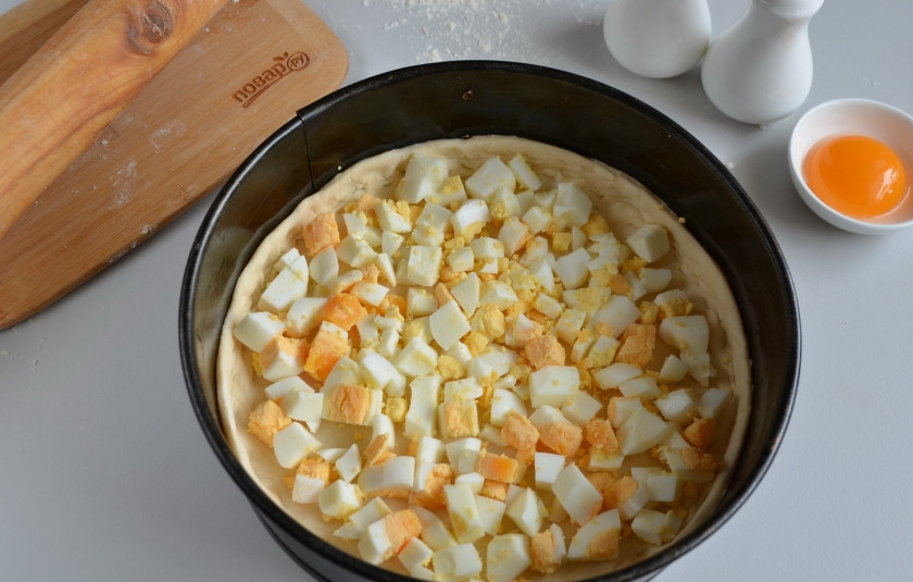 1. Этап. Слоеный пирог с семгой: Застелите форму бумагой, смажьте растительным маслом. Уложите тесто, придавите бортики к краю формы. Порубите крупно вареные яйца, равномерно распределите их по тесту.