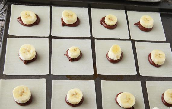 1. Этап. Треугольнички с Нутеллой и бананами: 3. Выложить пасту Нутелла в кондитерский мешок или обычный пластиковый мешок с прорезью в одном углу и выдавить небольшое количество шоколадной паты в центр каждого квадрата рисовой бумаги. При желании на пасту можно положить конфетку Hershey’s Kisses. Положить верху ломтик банана и слегка прижать пальцами.