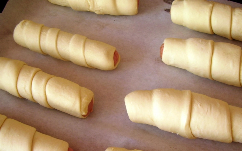 1. Этап. Сосиски в слоеном дрожжевом тесте в духовке: 3. Сосиски использую сырые, заворачиваю каждую в тесто (тесто закручиваю как будто по спирали). Взбиваю яйцо, смазываю им выпечку для получения румяной корочки.