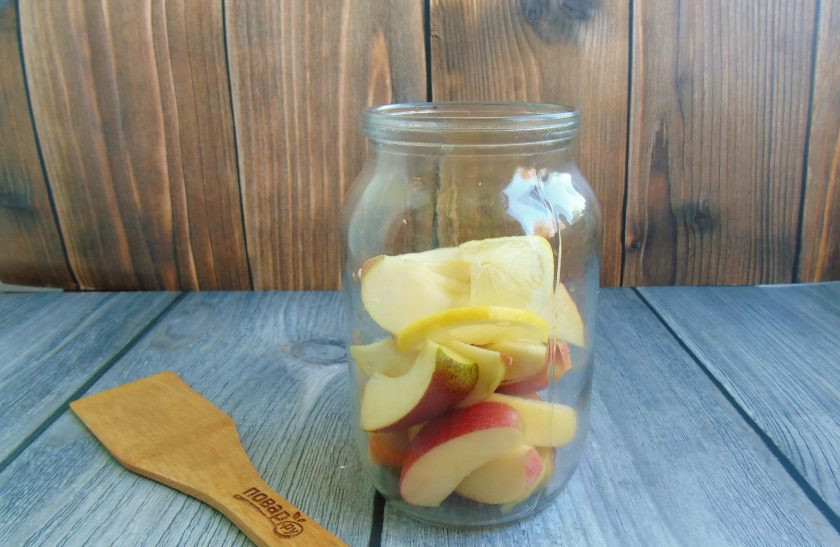 1. Этап. Компот из яблок и лимонов на зиму: Нарезанные яблоки выложите в стерилизованную банку. Лимон помойте и нарежьте половинками кружков. Добавьте в банку 1-2 дольки лимона.