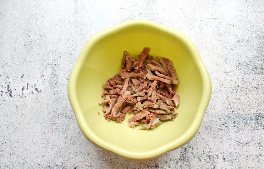 1. Этап. Салат Праздничный с говяжьим языком: Говяжий язык порежьте средней соломкой и выложите в салатник.