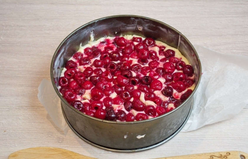 1. Этап. Бисквит с вишней: Форму застелите пергаментом. Стенки формы смажьте маслом. Выложите в форму тесто. Сверху заполните поверхность теста свежей вишней. Предусмотрительно удалите у вишни косточки. Вишен нужно очень много.