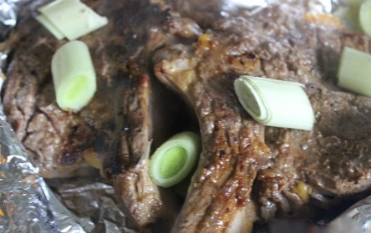 1. Этап. Запеченная корейка на кости: 4. На дно блюда для запекания выложите фольгу, лучше выложить её в несколько слоев, чтобы не вытек сок. Возьмите лук порей, хорошо промойте, белую часть порежьте небольшими кружочками. На фольгу аккуратно выложите замариновавшееся мясо, сверху посыпьте нарезанным пореем.