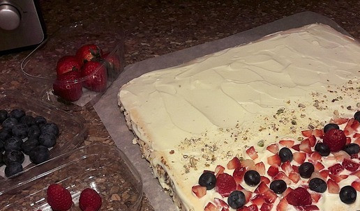 1. Этап. Меренговый рулет с ягодами и орехами: Достаньте меренгу из духовки и дайте ей немного остыть. Нарежьте свежую клубнику кубиками. Смажьте меренгу кремом, выложите на один край коржа клубнику, немного рубленых фисташек, и несколько ягод малины и голубики