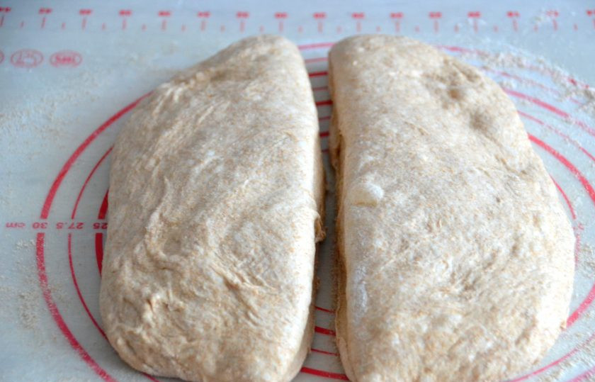 1. Этап. Чиабатта из цельнозерновой муки: Как только тесто поднимется после третьей обминки, присыпьте цельнозерновой мукой рабочую поверхность стола. Аккуратно выложите тесто, стараясь его больше не мять, чтобы сохранить в нем воздух. Слегка растяните тесто в прямоугольный пласт и разрежьте на 2 части.