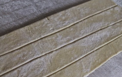 1. Этап. Трубочки с изюминкой: 4. Раскатайте пласт слоеного теста и разрежьте его на тонкие полоски (около 1-2 см в ширину).