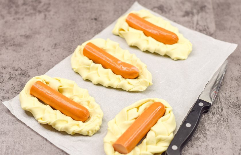 1. Этап. Плетеные Хот-доги из слоеного теста с плавленым сыром: Две длинные сосиски разрежьте пополам, выложите сосиски в центр плетенных заготовок.