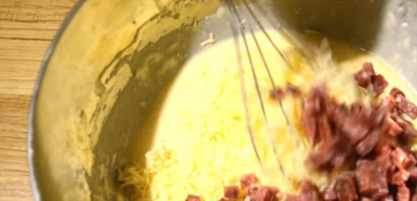 1. Этап. Закусочный кекс с сыром и колбасой: 2. Твердый сыр натрите на мелкой терке и добавьте к тесту. Колбасу нарежьте мелкими кубиками и добавьте к тесту, перемешайте. Посолите и поперчите по вкусу.