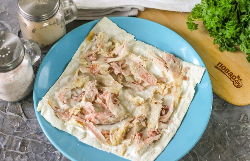 1. Этап. Закусочный торт Наполеон с курицей и грибами: Окорочок разберите руками, отделяя мясо от костей и разрывая его на волокна. Выложите на тарелку лист лаваша, смажьте его сметаной или майонезом любой жирности. На соус выложите части отварного куриного мяса.