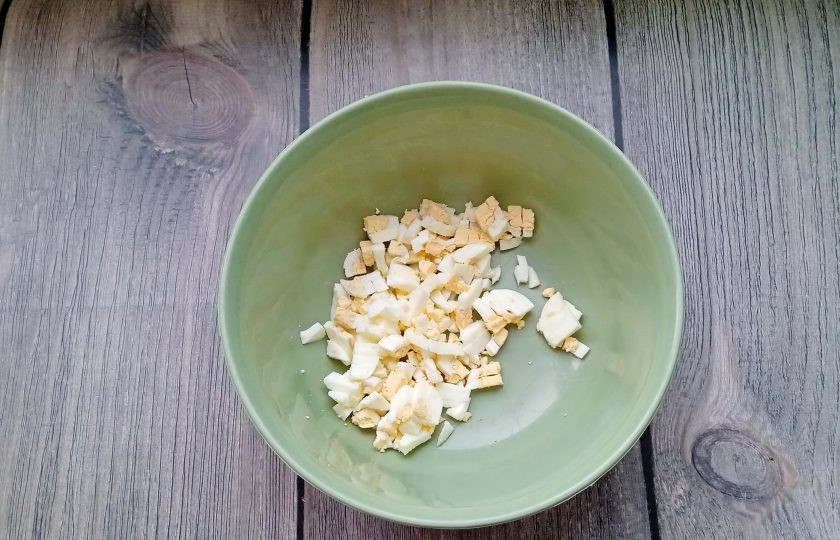 1. Этап. Салат из крабовых палочек с луком и зеленью: Яйца сварите вкрутую, охладите, очистите и мелко нарежьте. Выложите в миску.