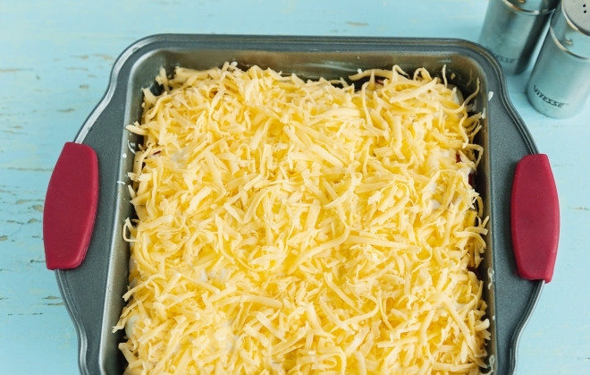 1. Этап. Каннеллони с куриным фаршем: Залейте противень с каннеллони сметаной. Обильно посыпьте тертым сыром.