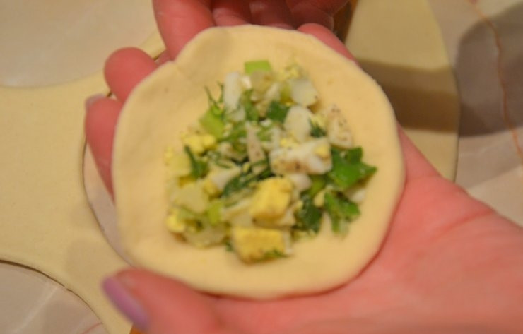 1. Этап. Пирожки с зеленым луком и яйцом: Тесто раскатайте на плоской поверхности, немного присыпав её мукой. Слой теста должен быть не более 2-3 миллиметров, чтобы пирожки хорошо прожарились и не подгорели. При помощи стакана вырежьте из теста кружки, на каждый положите по ложке начинки. Защипните пирожки по краям.