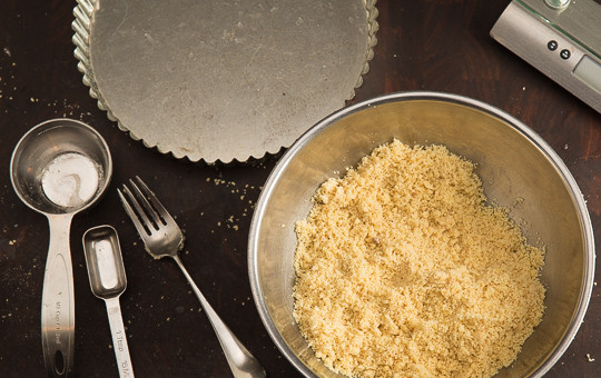 1. Этап. Грушевый пирог без глютена: 1. Первым делом включите духовку, разогрейте ее до 180 градусов. В глубокую мисочку отправьте сахар, соль, миндальную и кокосовую муку. Перемешайте. Растопите сливочное масло, понемногу добавляйте, перемешивая тесто. 2-3 ложки крошки отложите в сторону и продолжайте подливать масло.