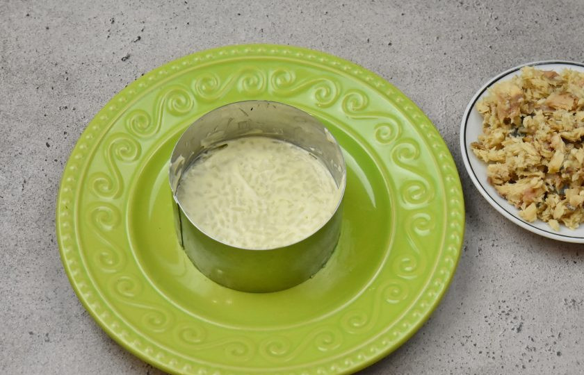 1. Этап. Пасхальный салат с консервированным лососем: Первым слоем выложите половину всего объема отварного риса. Каждый слой промазывайте небольшим количеством майонеза.