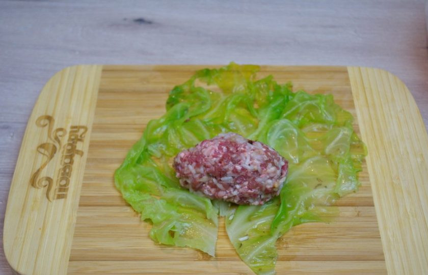 1. Этап. Голубцы с рисом: Фарш посолите и поперчите. Хорошо вымешайте. Кочан капусты разберите на листья. В глубокую кастрюлю сложите листья. Ошпарьте кипятком и прокипятите на огне около 5 минут, чтоб листья стали мягкими. Слейте воду с листьев. Остудите. Лист капусты уложите на стол. Твердую часть листика нужно вырезать острым ножом. На середину листика уложите порцию фарша, сформированную в виде котлетки.