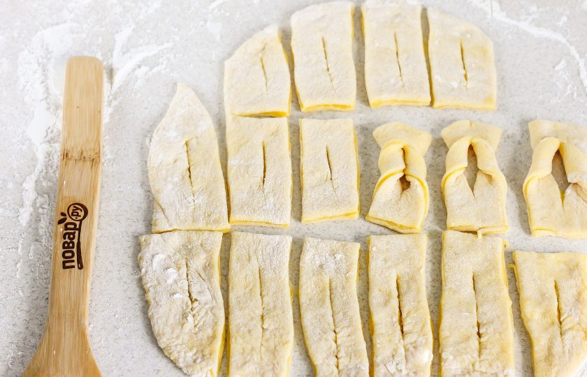 1. Этап. Хворост на коньяке: В середине каждого прямоугольника сделайте надрез, но не до конца, и проверните один край заготовки в разрез, выворачивая обратно. Такие манипуляции проделайте и с остальными заготовками.