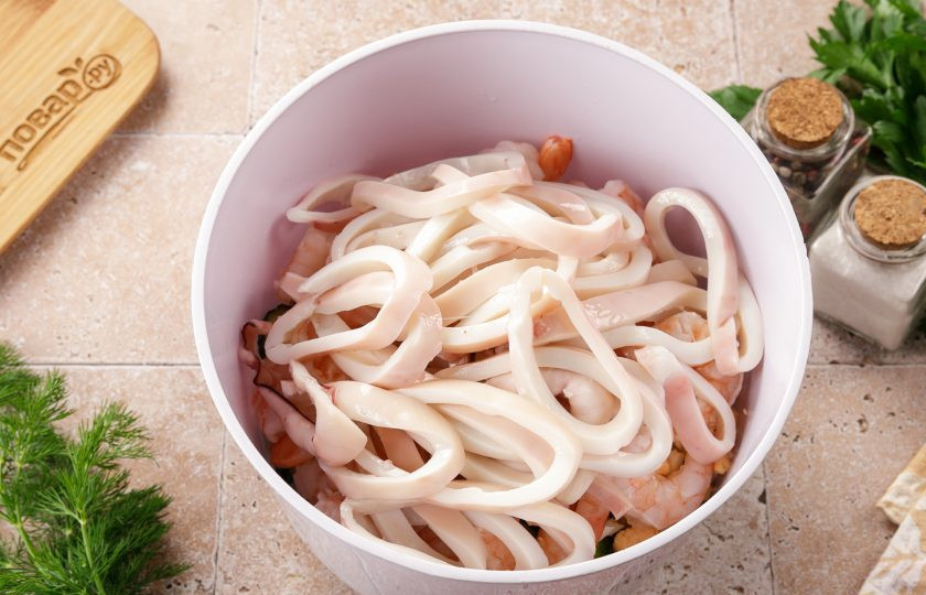1. Этап. Салат с кальмаром, креветками и огурцом: Остудив в холодной воде кальмары, тщательно вымойте их под проточной водой. Счистите с них плёнку, уберите с внутренней полости тушки хитиновую пластину. Сваренные и очищенные тушки кальмаров нарежьте тоненькими колечками, так кальмары будут особенно заметны в салате и акцент вкуса будет смещён именно в сторону морепродукта.