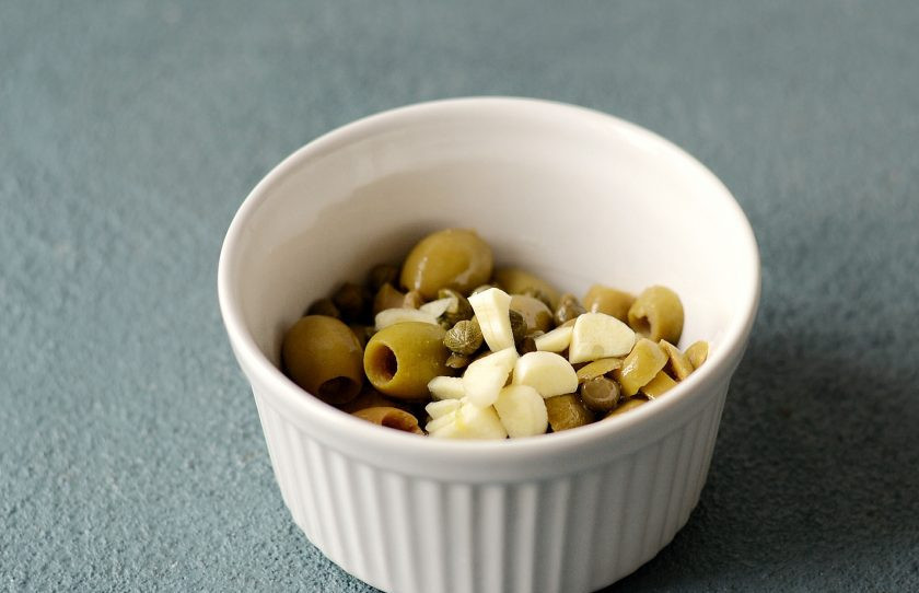 1. Этап. Оливковый паштет: Чеснок очистите от кожуры, нарежьте ломтиками, чтобы его было проще измельчать. Сложите все ингредиенты в одну емкость.