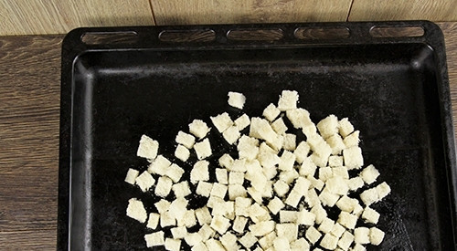 1. Этап. Простой рецепт Цезаря с курицей: Батон нарежьте кубиками, удалив корки. Выложите их на противень. Сбрызните батон маслом, убрав чеснок.