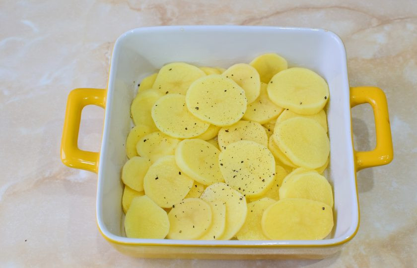 1. Этап. Мясо по-орловски из свинины: Форму для запекания смажьте растительным маслом. Очищенный картофель нарежьте кружочками и выложите по дну формы. Все слои по вкусу посыпайте солью и специями.