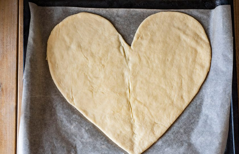 1. Этап. Пицца Сердце: Раскатайте тесто в пласт толщиной примерно в 3-4 мм. Очень удобно раскатать тесто на пергаменте для выпекания, а затем перенести его на противень. Затем воспользуйтесь любым удобным для вас шаблоном и вырежьте ножом для пиццы из теста форму в виде сердца. Я сделала основу для теста в виде сердца на весь противень, он у меня стандартных размеров.