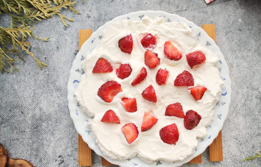 1. Этап. Торт из зефира с клубникой без выпечки: У клубники удалите хвостики, порежьте ее на кусочки. Разложите часть ягод поверх взбитых сливок.