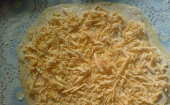 1. Этап. Булочки с сыром из слоеного теста: Разморозьте тесто. Раскатайте его в пласт. Толщина блина должна быть в несколько мм. (это важно). Смажете плавленым сыром или маслом. Натёртый сыр высыпьте на получившийся 