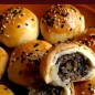 Слоёные колобки Приготовьте тесто 1. Смешайте масло с мукой, затяните пленкой, поставьте в холодильник на 30 минут Приготовьте тесто 2. Масло смешайте с мукой, сахар растворите в воде, замесите тесто. Затяните тесто пленкой, оставьте на 20 минут. Приготовьте начинку. Поджарьте кунжут и орехи. Орехи и часть кунжута измельчите блендером. Поджарьте муку. Нарежьте лук мелким кубиком. Мясо и сало мелко нарежьте, поджарьте. В сковороду с мясом введите лук, припустите. Введите в сковороду сухое вино и соевый соус, через 10 сек снемите с огня. Мясо, лук с жидкостью измельчите блендером. Смешайте все компоненты, регулируйте вязкость добавляя муку. Разделите начинку на шарики (размером 2 фундука). Выполните формовку пирожков: Разделите оба вида теста на 18 кусочков (9+9). Сформуйте из теста шарики, накройте плёнкой. Шарик из теста 2 раскатайте в тонкую лепёшку, в центр поместите шарик из теста 1. Защипите края лепёшки. Сформируйте цилиндр. Приплюсните цилиндр пальцами (равномерно распределяйте тесто 1 внутри теста 2, шов должен быть сверху), раскатайте. Сверните