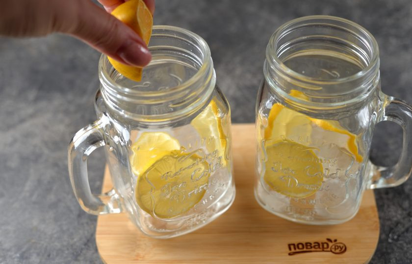 1. Этап. Лимонад «Киви»: Сразу подготовьте два удобных стакана. Помойте и вытрите насухо лимон. Половину нарежьте тонкими кружочками, из второй половины выдавите сок прямо в стаканы. Выложите немного льда в каждую порцию.