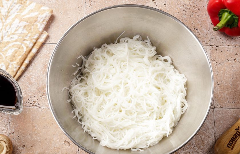 1. Этап. Фунчоза с курицей и шампиньонами: Фунчозу отправьте в глубокую кастрюлю (или миску), залейте кипятком (500 мл.). Накройте крышкой и оставьте на 5-6 минут. Затем слейте горячую воду и промойте стеклянную лапшу холодной водой, откинув на дуршлаг. После того, как вода стечёт, переложите в глубокую миску или сразу в салатник.