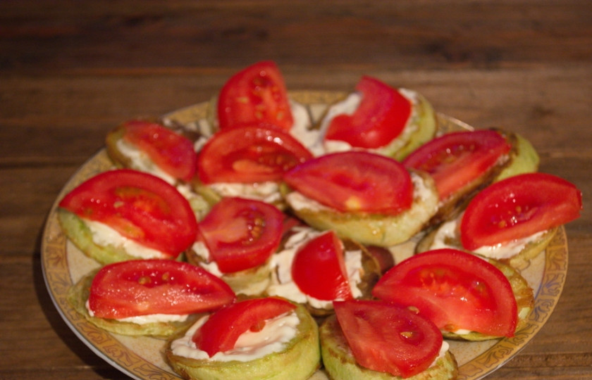 1. Этап. Жареные кабачки с помидорами и сыром: Смажьте кабачки смесью майонеза и чеснока. Вместо майонеза можно использовать сметану, но в нее следует добавить соль, специи по вкусу. На каждый кусочек кабачка выложите по кусочку помидора.