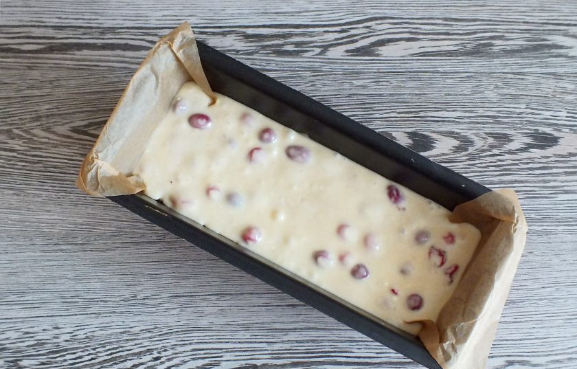 1. Этап. Кекс с клюквой на сметане: Форму для кекса выстелите пекарской бумагой. Перелейте в неё тесто. Разровняйте лопаткой. Посередине проведите 